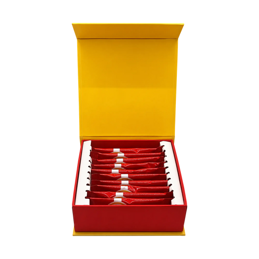 An open red gift box with a bright yellow interior lid, containing multiple small red sachets arranged in rows on a white insert, photographed on a plain white background.